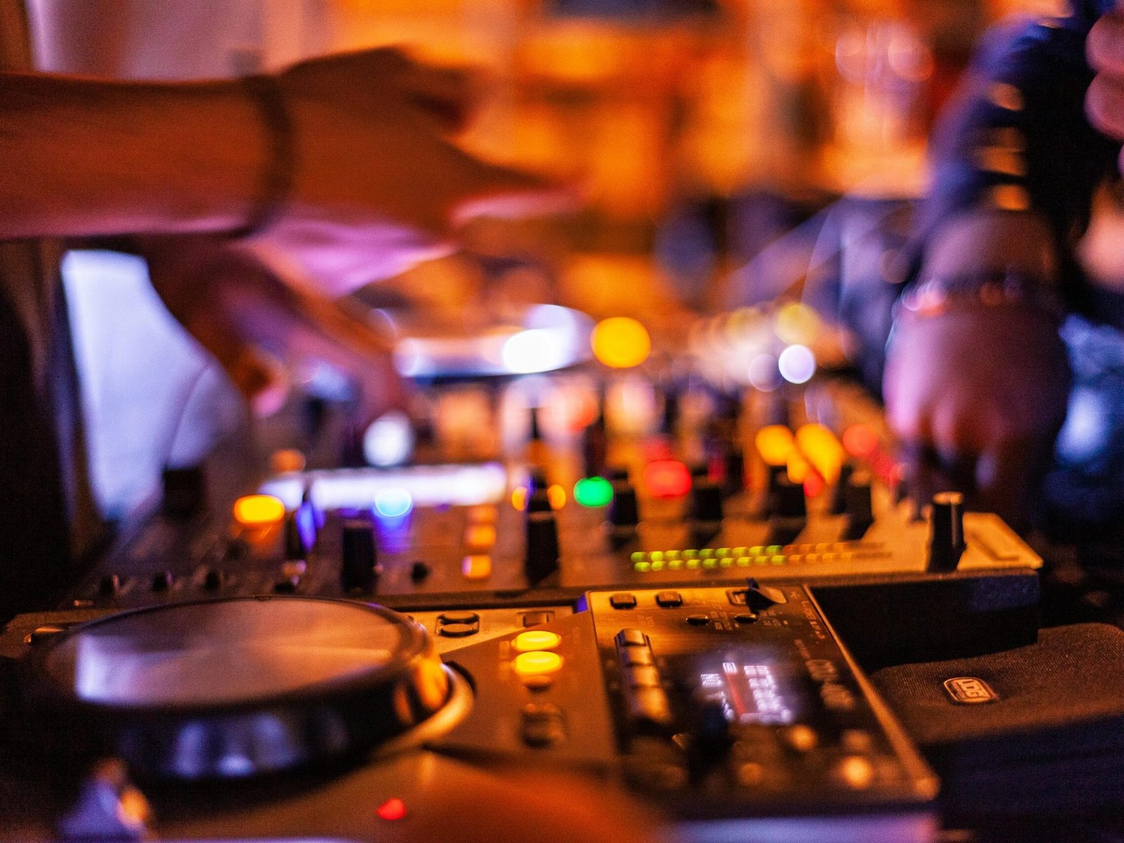 Close-up of DJ mixing console with hands adjusting controls at a lively nightclub.